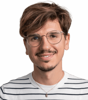 Ein junger Mann mit hellbraunem Haar und Brille lächelt in die Kamera. Er trägt ein weißes Hemd mit schwarzen Streifen und eine Halskette vor einem schlichten weißen Hintergrund.
