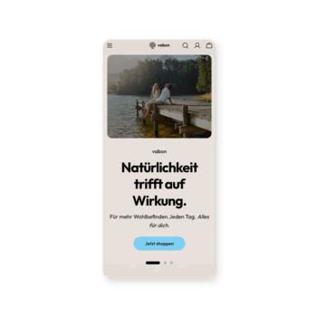 Auf dem Bildschirm eines Mobiltelefons wird eine Website mit einem Foto von zwei Personen angezeigt, die auf einem Steg an einem See sitzen. Unter dem Bild steht der deutsche Text